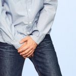A man in jeans covers his crotch with both hands